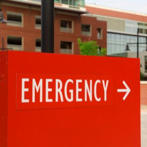 Bright red side that says Emergency in white letters. There is a red brick building in the background.